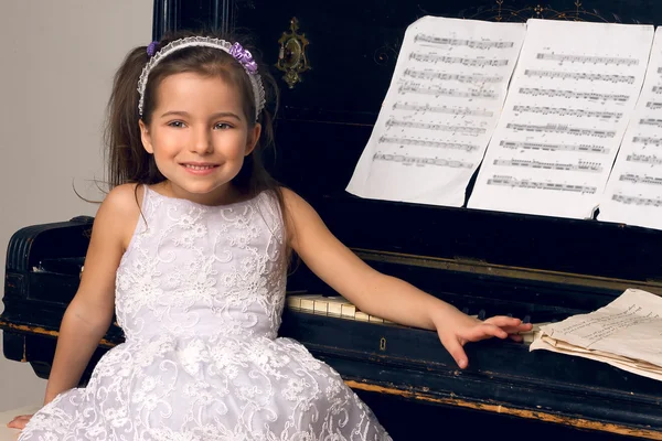 Ragazza in un bel vestito si siede al pianoforte — Foto Stock