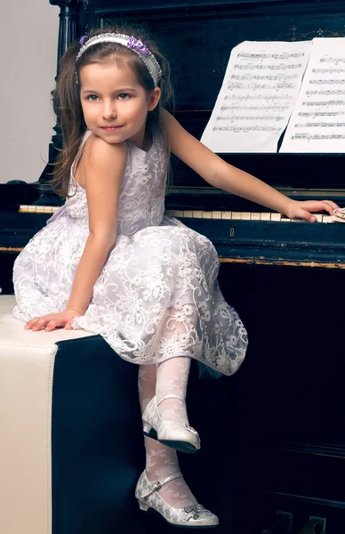 美しい衣装を着た少女はピアノに向かってすわり — ストック写真