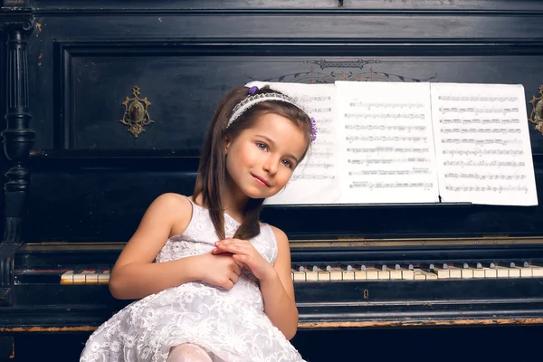 Jente i en vakker kjole sitter ved pianoet – stockfoto