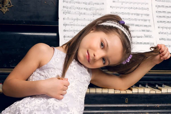 Flicka i en vacker klänning sitter vid pianot — Stockfoto