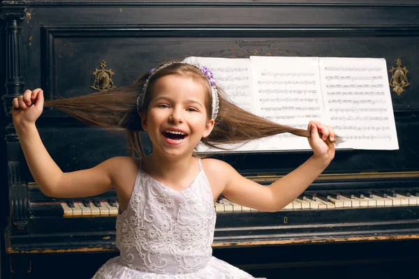 Mädchen in einem schönen Kleid in der Nähe des Klaviers glücklich — Stockfoto