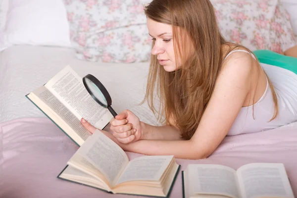 Mulher ler livro na cama com uma lupa — Fotografia de Stock