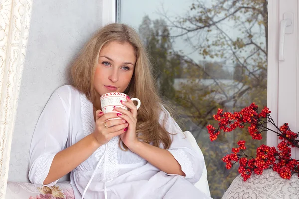 Chica sosteniendo taza y mirando a través de la ventana — Foto de Stock