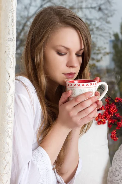 Girl holding cup and looking through window — Stock Photo, Image