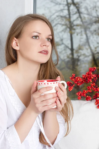 Ragazza in possesso di tazza e guardando attraverso la finestra — Foto Stock