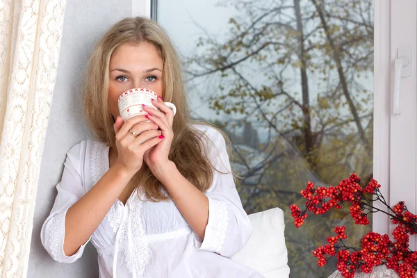 Girl holding cup and looking through window — Stock Photo, Image