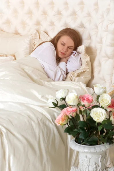 Schöne schlafende Frau im Bett mit Rosen — Stockfoto