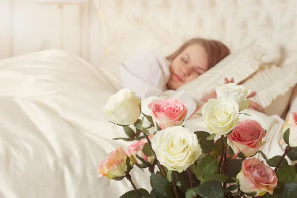 Schöne schlafende Frau im Bett mit Rosen — Stockfoto