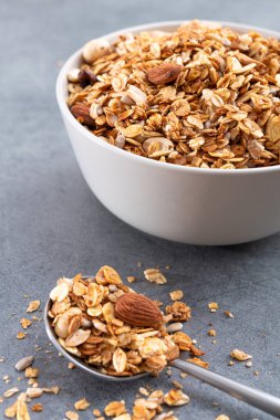 Beyaz kasede badem bulunan taze granola. Taş grisi arka plan. Kahvaltı yemeği. Dikey fotoğraf.