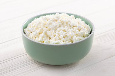 Beyaz ahşap bir masada, kasede saf süzme peynir. Sağlıklı gıda geçmişi.