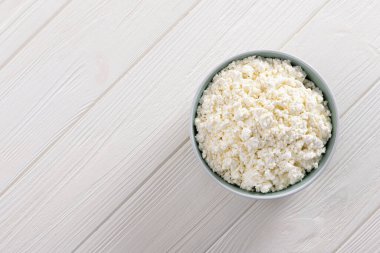 Beyaz ahşap bir masada, kasede saf süzme peynir. Sağlıklı yemek geçmişi. Üst görünüm.