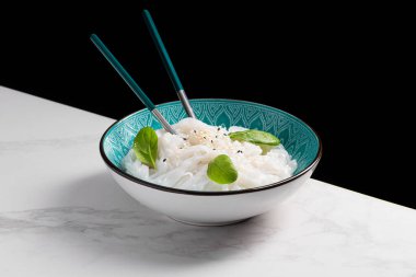 Taze ıspanak yapraklı bir kasede haşlanmış pirinç eriştesi. Çanak mermer bir levhanın üzerinde duruyor, siyah arkaplan. Doğu ve Güney Asya mutfağı. 