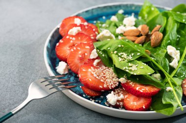 Fresh salad with strawberry fruit, almond, spinach and cottage cheese on a plate. concrete background. Diet and vegan food.
