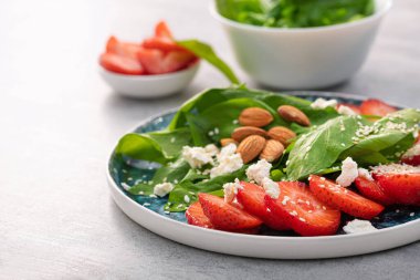 Fresh salad with strawberry fruit, almond, spinach and cottage cheese on a plate. concrete background. Diet and vegan food.