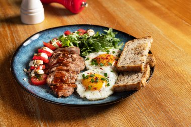 Morning breakfast with fried eggs, toast, steak, arugula, cherry tomatoes and mozzarella cheese. A delicious Italian snack in a cafe.