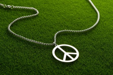 Metal bir madalyon, yeşil çimlerin üzerinde barış sembolü şeklinde bir kolye. Özgürlük kavramı. Ukrayna 'daki savaşı durdurun..
