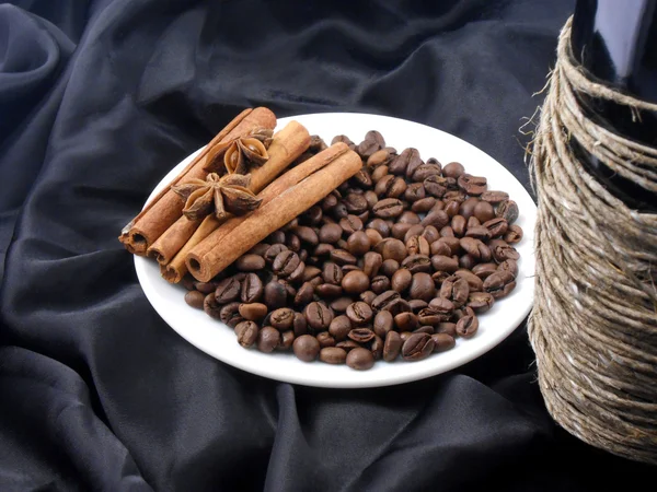 Champagne bottle, coffee beans, cinnamon and star anis on black material — Stock Photo, Image