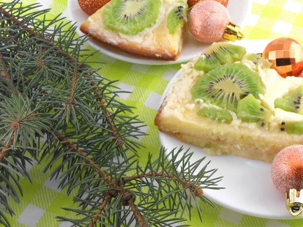 Pastel de kiwi en el plato con bolas de Navidad y árbol de año nuevo —  Fotos de Stock