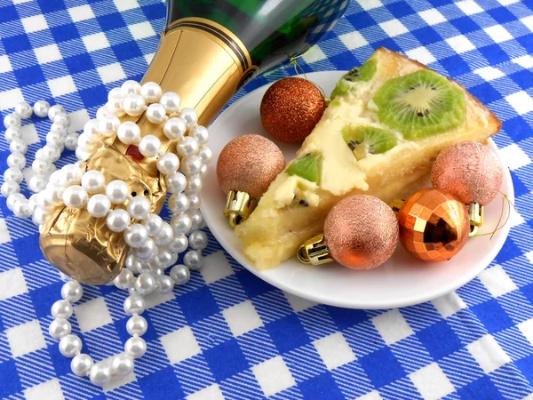 Kiwi bolo saboroso perto da placa, garrafa de champanhe, diamantes e bolas de Natal — Fotografia de Stock