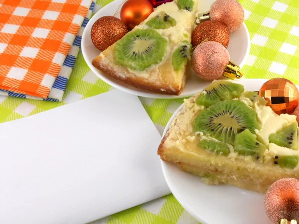 Kiwi cake on plate with white blank paper and christmas balls set — Stock Photo, Image