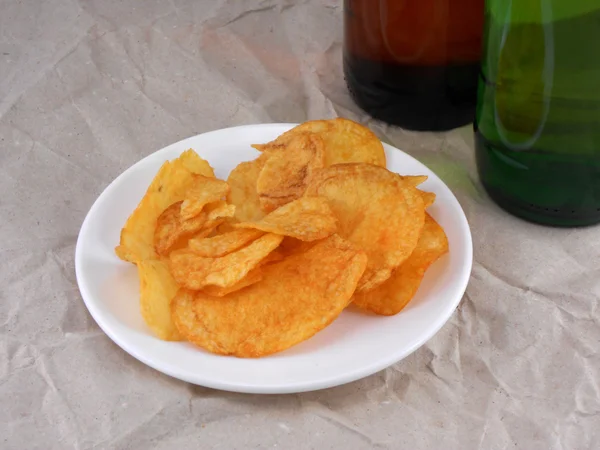 Bierflasche und Kartoffelchips auf weißem Teller — Stockfoto