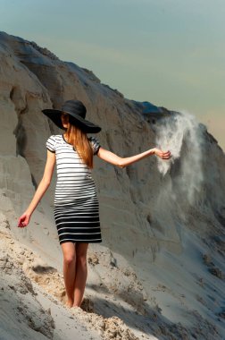 Genç bayan, kumun üzerinde şapka ve elbise giymiş..