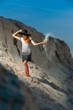 Genç bayan, kumun üzerinde şapka ve elbise giymiş..