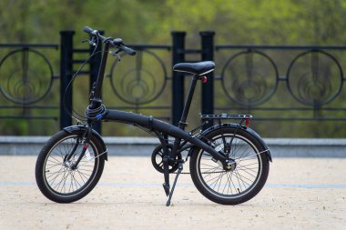 Folding black bike in the city park in summer.