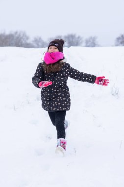 A little girl runs in the snow in winter.