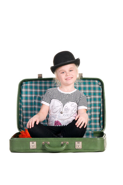 child sitting in an old green suitcase in anticipation of travel