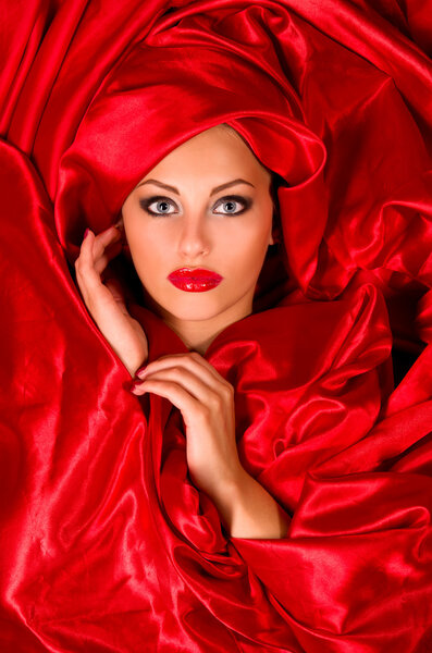 Sexy sensual face with aggressive make-up in red satin fabric