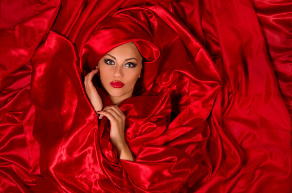 Sexy sensual face with aggressive make-up in red satin fabric