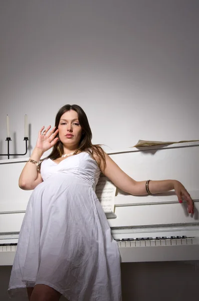 Беременная женщина возле белого фортепиано — стоковое фото