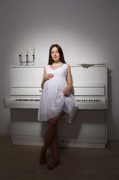 Kobieta w ciąży w pobliżu biały fortepian — Zdjęcie stockowe