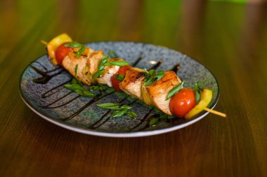 Çeri domatesli ızgara tavuk şiş, yeşil sebze ve kahverengi ahşap arka planda tabak sosu.
