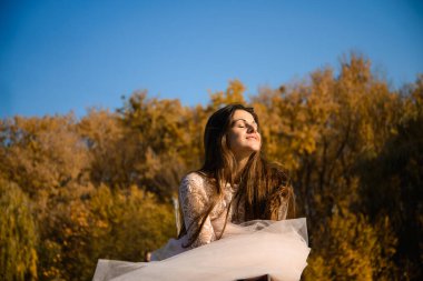 Açık bulutsuz bir günde açık pembe balo elbisesi içinde uzun siyah saçlı bir kız köprüde duruyor, şifon kumaş rüzgarda uçuşuyor. Sonbahar güneşine yüzünü gösterir.