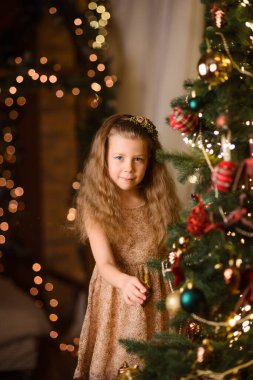 Mutlu çocuk odada bir Noel ağacı süsler, yeni yıl lambaları arka planda sarı bokeh verir.