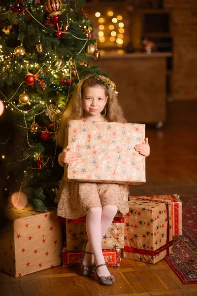 幸せな女の子はクリスマスツリーの下に座って 彼女の手に新年のギフトボックスを保持し 部屋のロフトのインテリアで — ストック写真