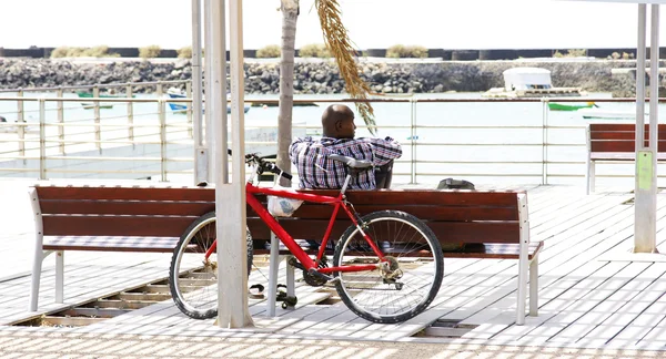 Homem negro descansando em um banco com bicicleta atrás — Fotografia de Stock