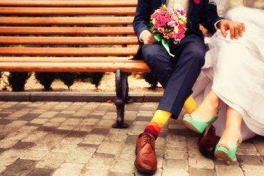 Bride and groom in bright clothes on the bench clipart