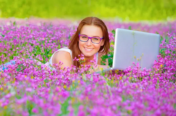 Pretty woman with laptop on floral field — Zdjęcie stockowe