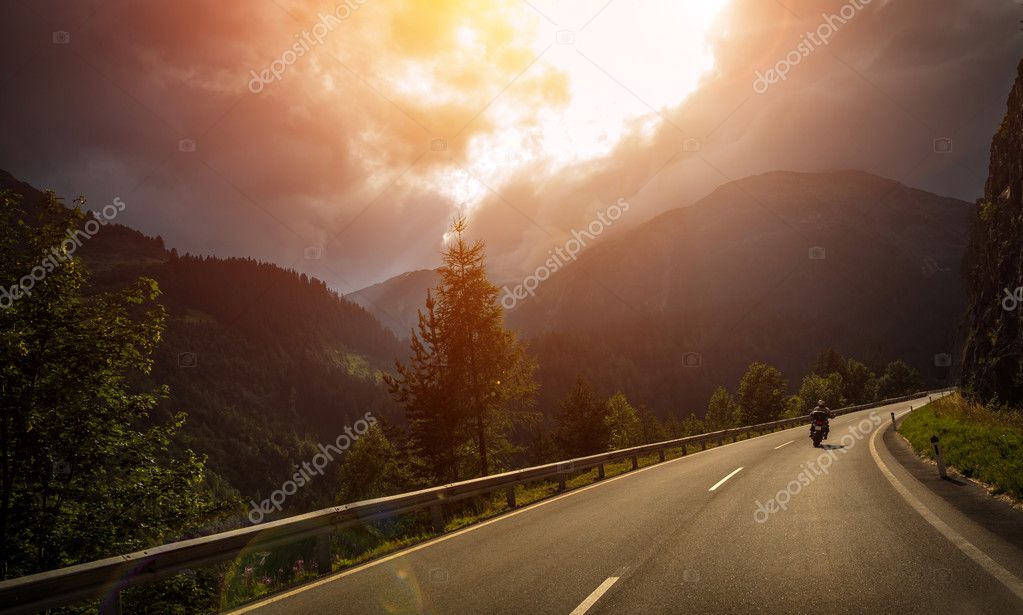 Motorcyclist in action, bright red sunset light, overcast weather, active lifestyle, traveling along Alpine mountains, extreme adventure concept