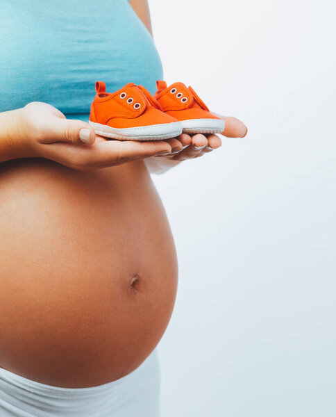 Closeup Photo of a Tummy of Pregnant Woman with Sweet Tiny Red Childs Boots isolated on White Background. Happy Pregnancy Time.