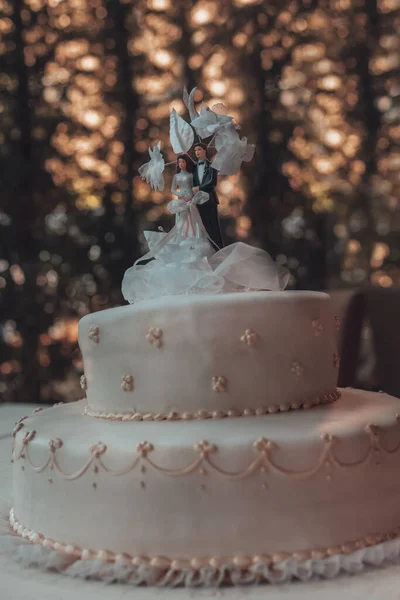 Photo of a Tasty Wedding Cake with Traditional Wedding Toys on Top. Ceremony Outdoors. Bride and Groom Dolls. New Family Concept.