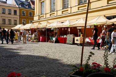 Lublin, Polonya - 11 Eylül 2021: Tedarikçilerin tezgahları eski kasaba meydanındaki binalardan birinin yanına dizilmişti. Asfalt kaldırımda ilginç bir yeri ziyaret eden insanlar var.