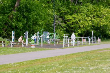 Gdynia, Polonya - 24 Mayıs 2022: Çeşitli ekipmanlı açık hava spor salonu gezinti güvertesinde, ağaçlara yakın. Spor aktiviteleriyle ilgilenen üç kişi var.