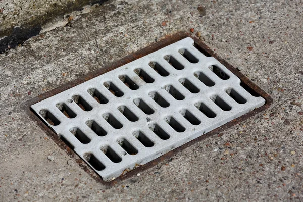 A storm drain grate in the sidewalk is made of plastic placed in the sidewalk