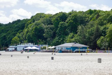 Gdynia, Polonya - 3 Haziran 2022: Arka planda yoğun yaprak döken ağaçlar var ve onların yanında, plajın yanında, tek katlı restoran binaları var.
