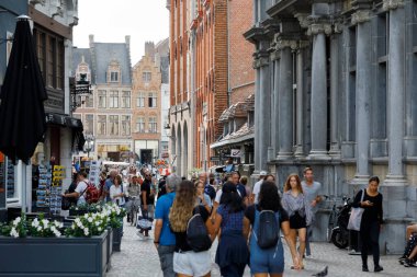 Bruges, Belçika - 7 Eylül 2022: Birçok insan dar, asfalt cadde boyunca kasaba meydanına doğru yürüyor. Meydanda da çok sayıda insan var ve tuğla evler görülebilir durumda.
