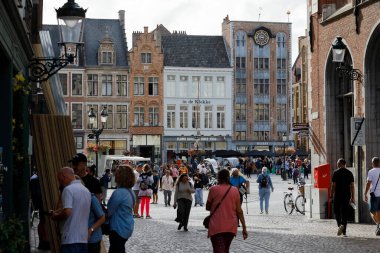 Bruges, Belçika - 7 Eylül 2022: Kasaba meydanındaki kalabalık şehrin tarihi kısmını araştırıyor. Bu meydanın önünü oluşturan tuğla evleri yan yana görebilirsiniz.